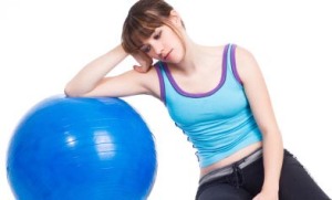 Young woman lying down on a blue exercise ball looking sad and tired